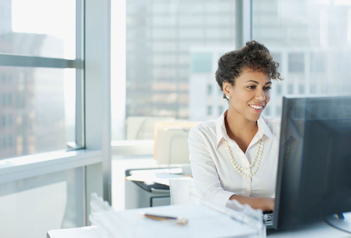 Female in office highrise, checking computer for unclaimed property, modern windows